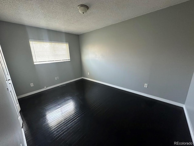 empty room featuring visible vents, dark wood-style floors, baseboards, and a textured ceiling