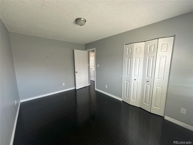 unfurnished bedroom with dark wood finished floors, a textured ceiling, a closet, and baseboards