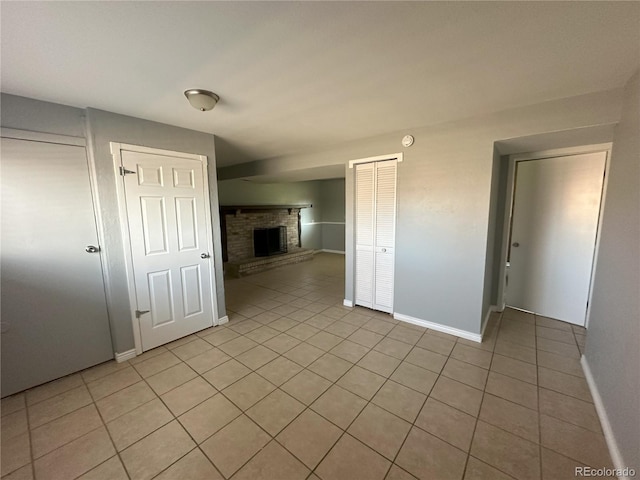 unfurnished room with light tile patterned flooring, a brick fireplace, and baseboards