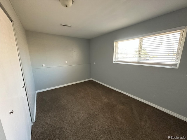 empty room featuring baseboards, visible vents, and dark carpet