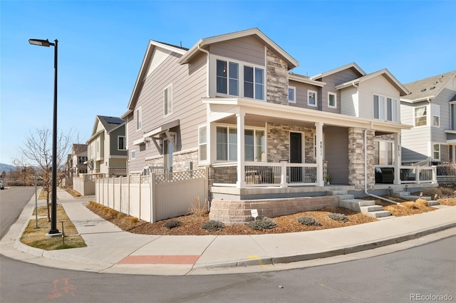 view of front of house featuring a fenced front yard, stone siding, covered porch, and a residential view