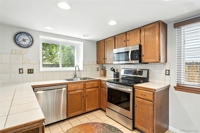 8468 S Upham Way, Littleton, CO 80128 - kitchen with appliances with stainless steel finishes, tile counters, decorative backsplash, brown cabinetry, and light tile patterned floors