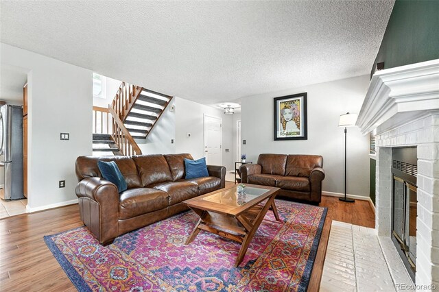 8468 S Upham Way, Littleton, CO 80128 - living room featuring stairway, light wood-style floors, a textured ceiling, and a brick fireplace
