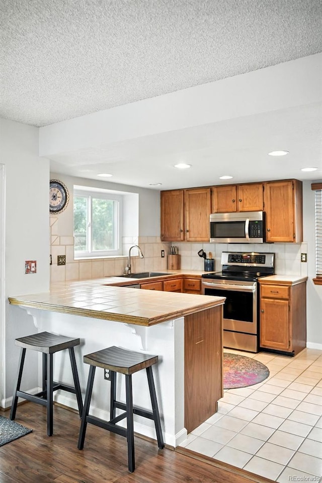 8468 S Upham Way, Littleton, CO 80128 - kitchen featuring appliances with stainless steel finishes, a peninsula, decorative backsplash, a breakfast bar, and light countertops
