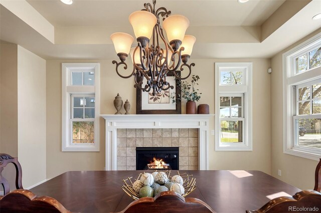 dining area with an inviting chandelier, a raised ceiling, and a tile fireplace