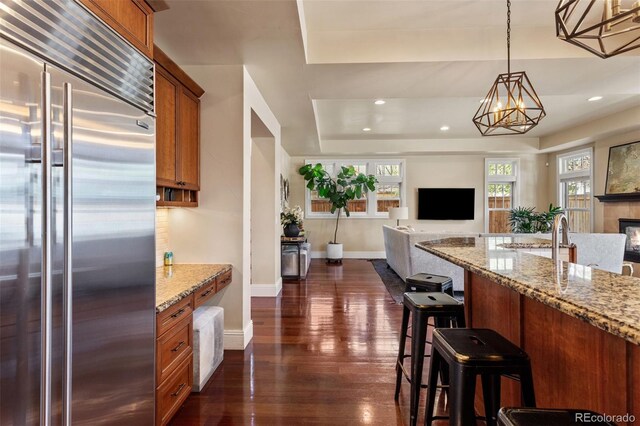 kitchen featuring brown cabinets, dark wood-style flooring, built in refrigerator, and open floor plan