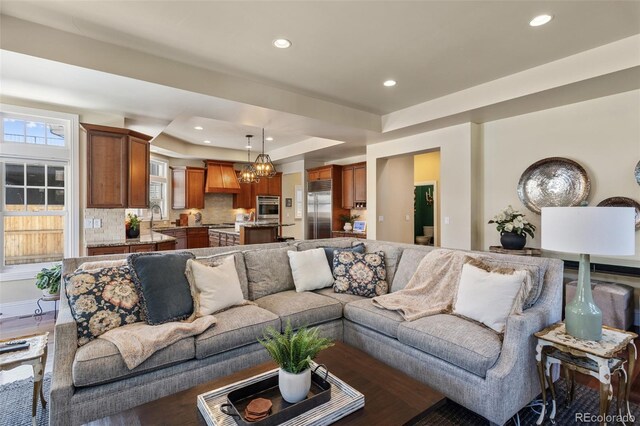 living area featuring an inviting chandelier, a tray ceiling, recessed lighting, and wood finished floors