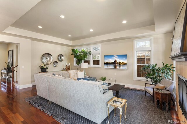living area with dark wood-style flooring, a fireplace, baseboards, recessed lighting, and a raised ceiling