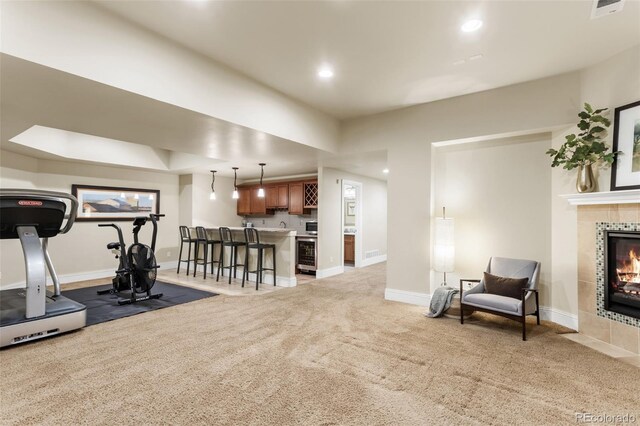 workout room featuring baseboards, beverage cooler, light carpet, and a tile fireplace