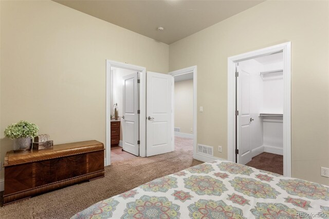 carpeted bedroom featuring baseboards, visible vents, ensuite bathroom, and a spacious closet