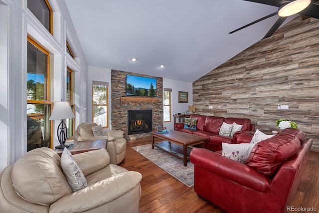 living area with high vaulted ceiling, wood walls, a fireplace, wood finished floors, and a ceiling fan