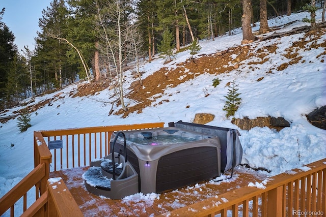 snowy yard with a wooded view, a hot tub, and a wooden deck