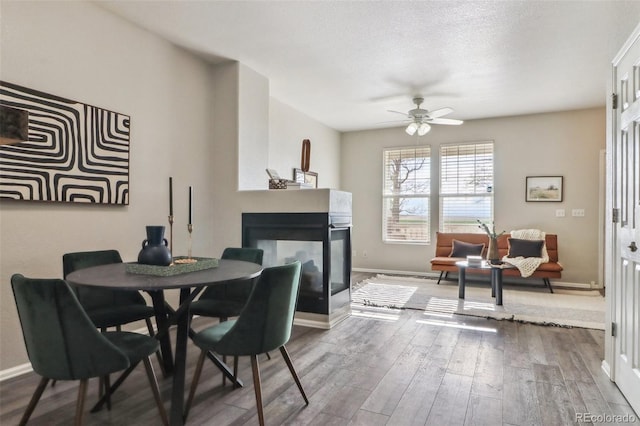 15612 E 96th Way Unit 13E, Commerce City, CO 80022 - dining space with a multi sided fireplace, wood finished floors, ceiling fan, and baseboards