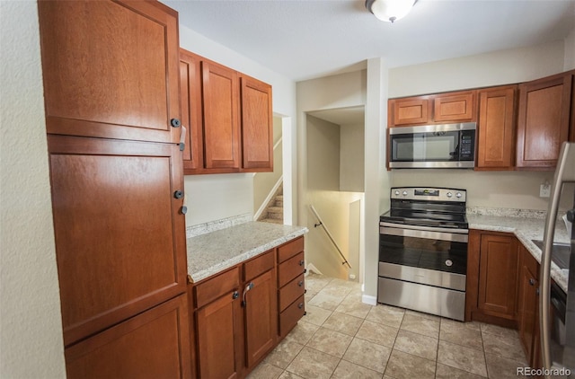 kitchen with appliances with stainless steel finishes, light stone counters, and light tile patterned flooring