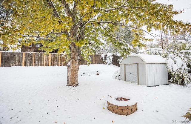 snowy yard with a storage shed and a fire pit