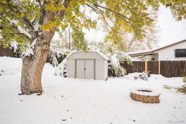 yard layered in snow with a shed and an outdoor fire pit