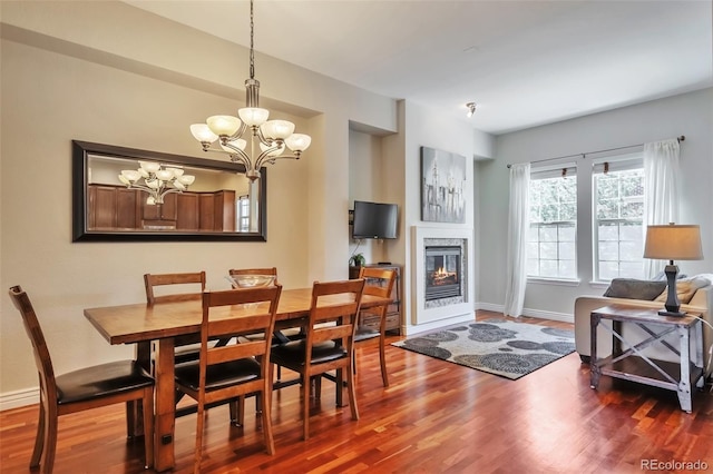 dining room with wood finished floors, a chandelier, a glass covered fireplace, and baseboards