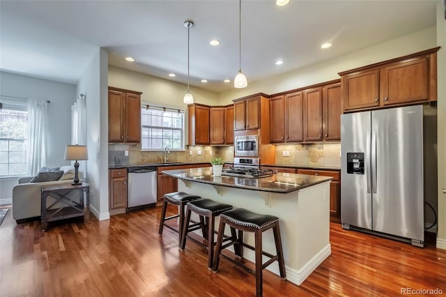 kitchen with stainless steel appliances, a sink, dark wood-style flooring, dark countertops, and recessed lighting