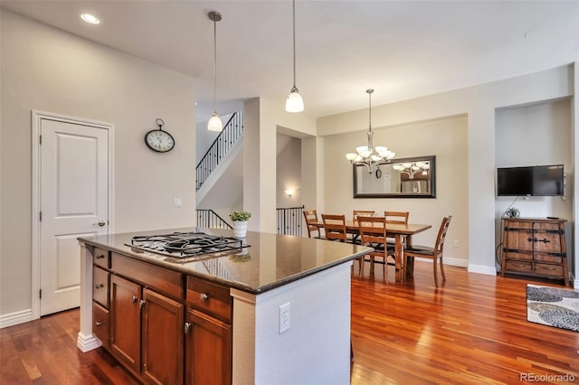 kitchen featuring dark wood-style floors, stainless steel gas stovetop, decorative light fixtures, baseboards, and a kitchen island
