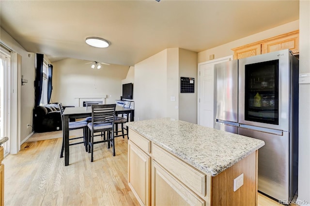 kitchen featuring a ceiling fan, a kitchen island, refrigerator with glass door, light wood-style floors, and light brown cabinets