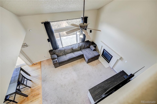 living area featuring a textured ceiling, wood finished floors, a glass covered fireplace, and a ceiling fan