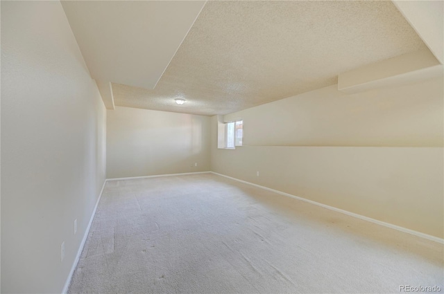 spare room with light colored carpet, a textured ceiling, and baseboards