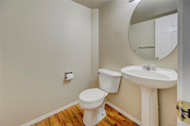 half bath with toilet, baseboards, and wood finished floors