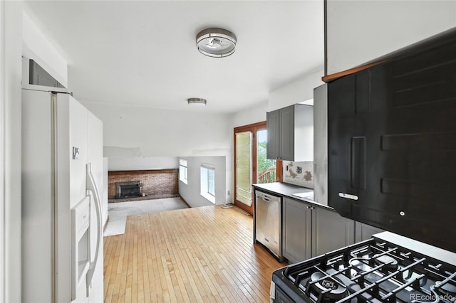 2527 S Ouray Way, Aurora, CO 80013 - kitchen featuring gas stove, white refrigerator with ice dispenser, stainless steel dishwasher, open floor plan, and a brick fireplace