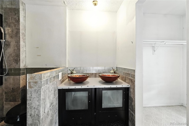 2527 S Ouray Way, Aurora, CO 80013 - bathroom featuring double vanity, a tile shower, a textured ceiling, and tile walls