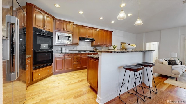 203 S Jackson St, Denver, CO 80209 - kitchen with appliances with stainless steel finishes, under cabinet range hood, light wood-style floors, a kitchen bar, and tasteful backsplash