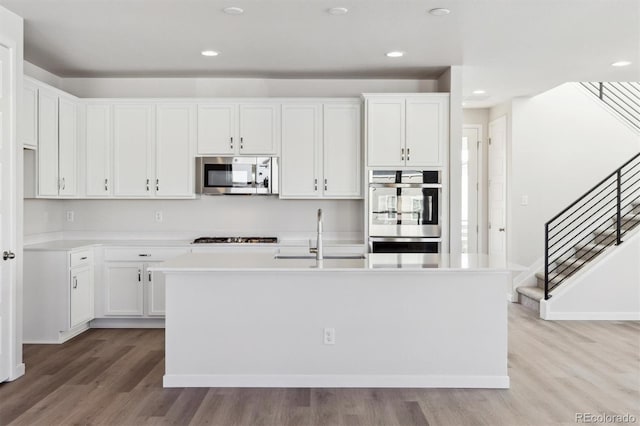 kitchen with white cabinetry, stainless steel appliances, a kitchen island with sink, and sink