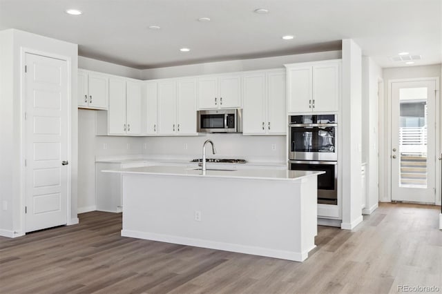 kitchen with appliances with stainless steel finishes, a center island with sink, white cabinets, and light hardwood / wood-style floors