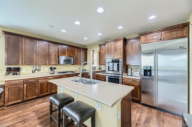 16059 E Grass River Pl, Parker, CO 80134 - kitchen with stainless steel appliances, wood finished floors, recessed lighting, a kitchen island with sink, and light countertops