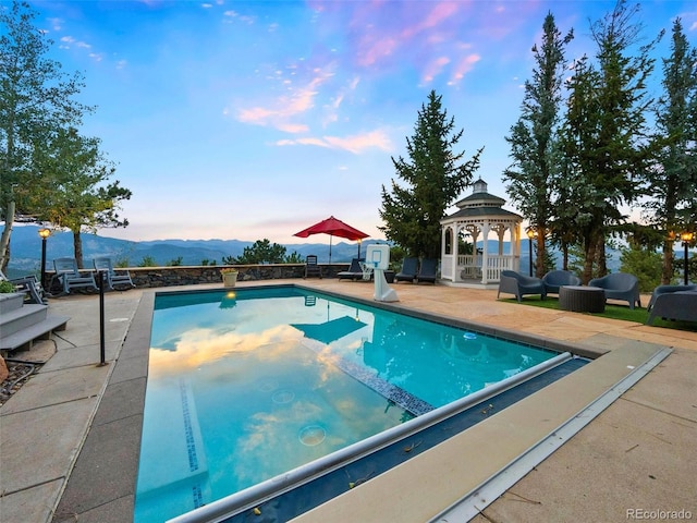 pool at dusk featuring a patio area and a gazebo