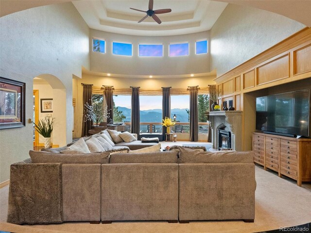 living room with a high ceiling, a tray ceiling, ceiling fan, and carpet