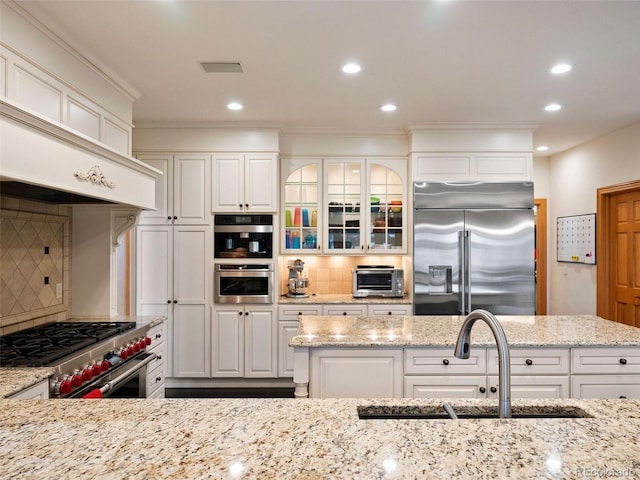 kitchen with a sink, decorative backsplash, high quality appliances, and white cabinetry