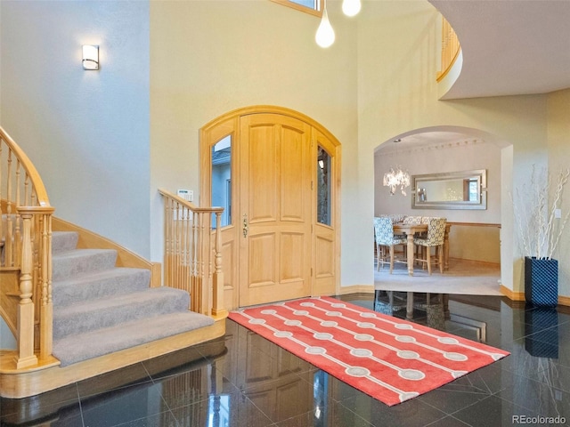 foyer featuring baseboards, granite finish floor, arched walkways, stairs, and a towering ceiling