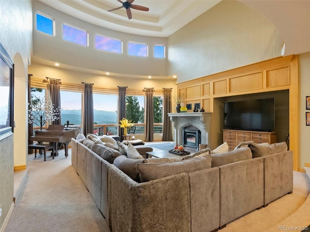 carpeted living room with a raised ceiling, a high ceiling, and ceiling fan