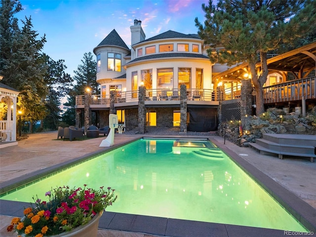 back house at dusk featuring a balcony and a patio