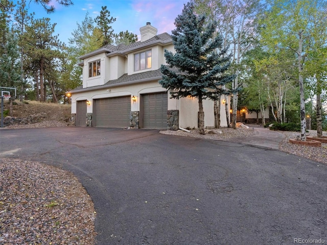 view of front of home with driveway, a chimney, stucco siding, stone siding, and a garage