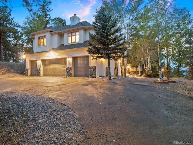 view of front of house featuring stucco siding, driveway, a chimney, and a garage