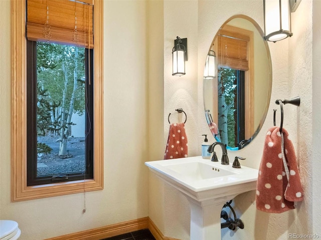 half bathroom featuring toilet, baseboards, and a sink