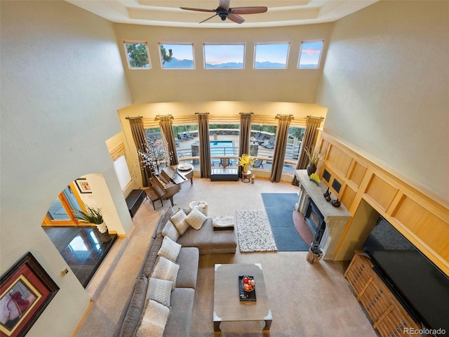 carpeted living room featuring a towering ceiling, a healthy amount of sunlight, and ceiling fan