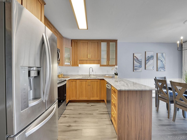 kitchen with sink, light hardwood / wood-style flooring, stainless steel appliances, light stone counters, and kitchen peninsula