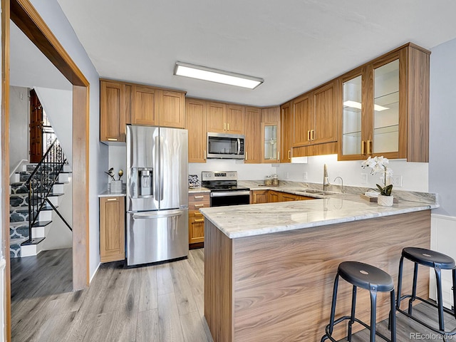 kitchen with sink, stainless steel appliances, light hardwood / wood-style floors, light stone countertops, and kitchen peninsula