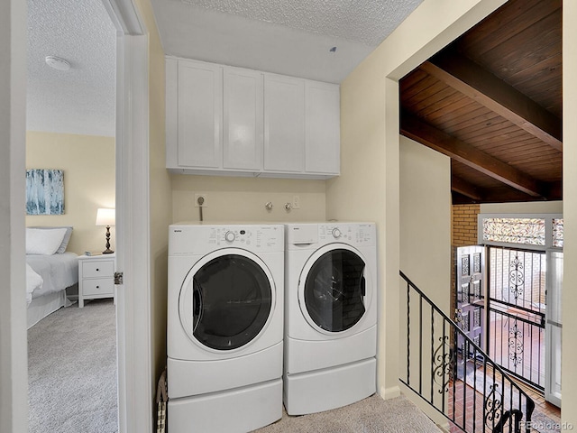 washroom with cabinets, light colored carpet, a textured ceiling, and washer and clothes dryer