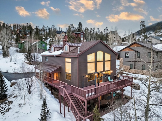 snow covered property featuring metal roof, a residential view, a wooden deck, and a standing seam roof