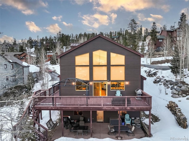 snow covered back of property with a patio and a deck