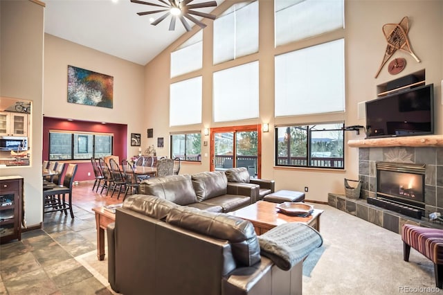 living area featuring a tiled fireplace, a ceiling fan, baseboards, and high vaulted ceiling