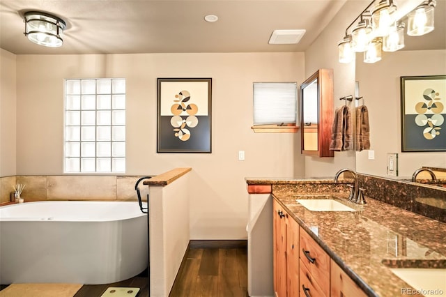 bathroom with a soaking tub, wood finished floors, double vanity, and a sink